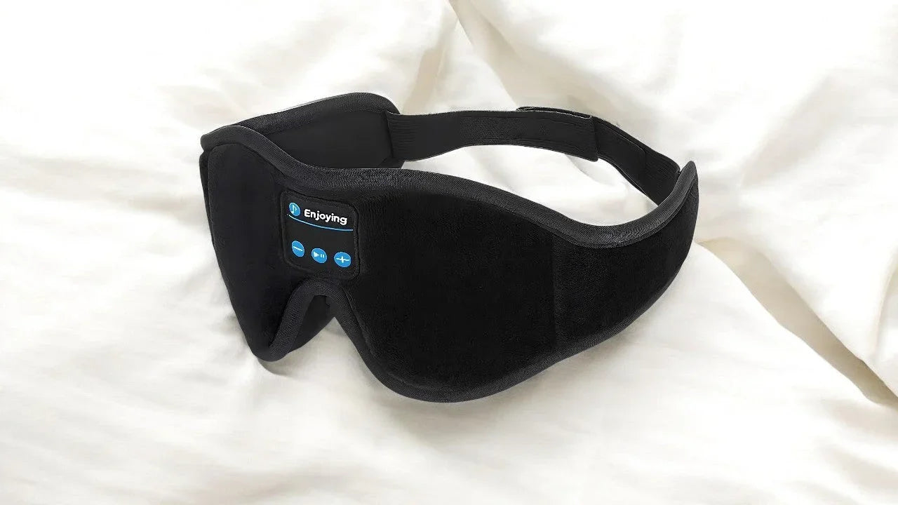 Masque de sommeil noir Bluetooth avec commandes intégrées posé sur un drap blanc